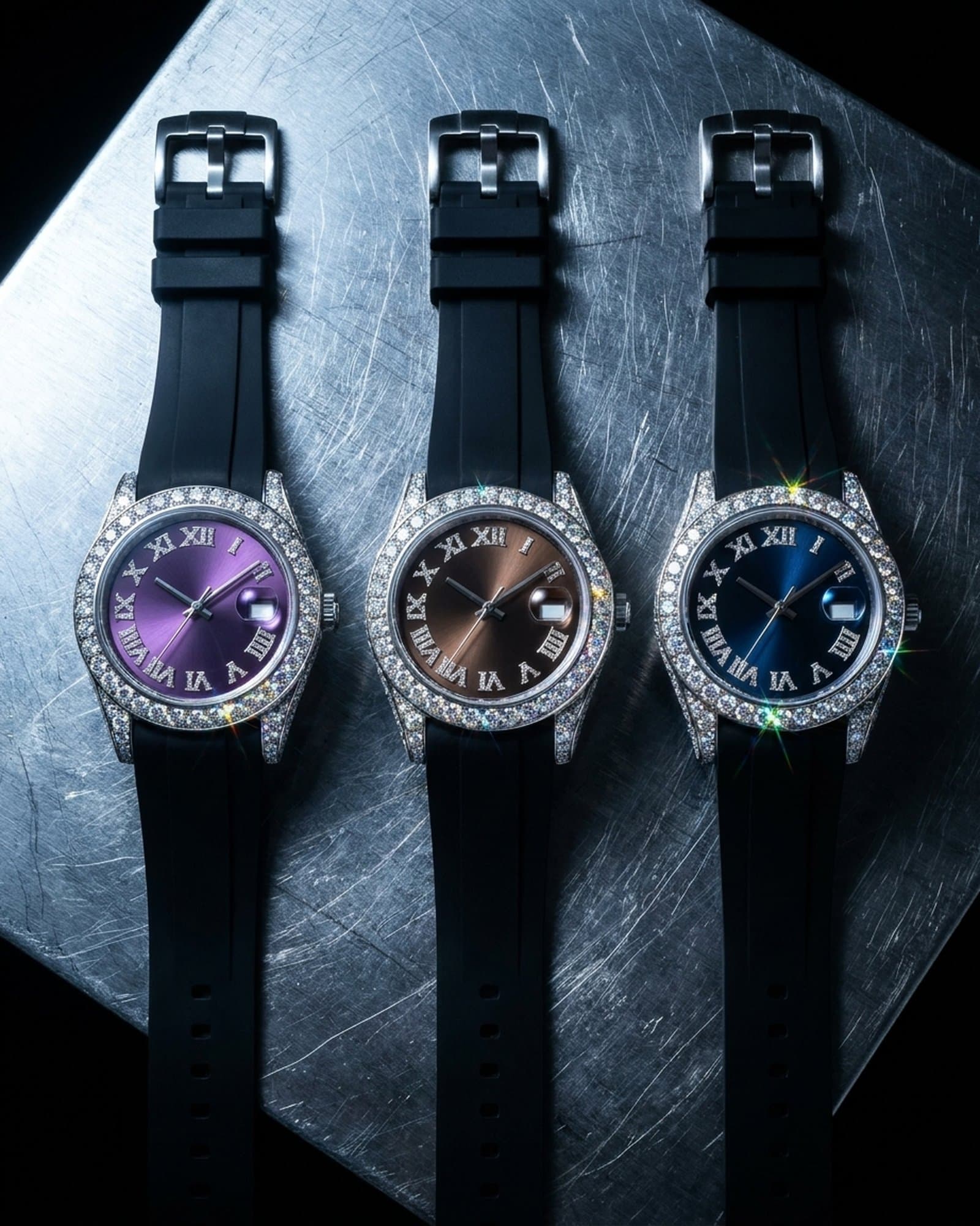 Three iced round watches on black rubber straps with purple, brown, and blue dials in a row on scratched steel